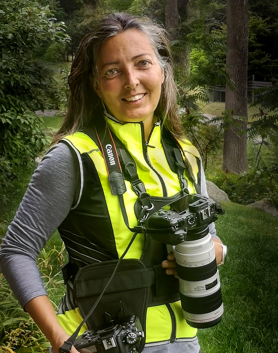 EdiCarboPhotosPicture Photo portrait de Edith Carbonneau de chez EdiCarbo Photographe portant sur elle ses boîtiers de caméras et lentilles professionnelles dans un décor naturel en forêt